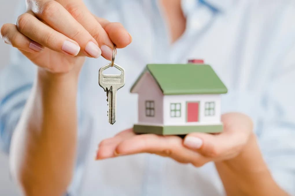 Person holding keys in one hand and a toy house in the other hand.