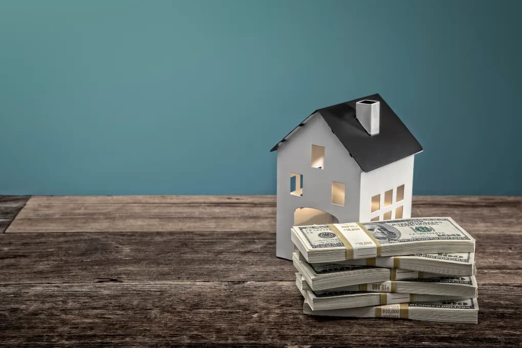 Toy house and stack of cash sitting on a table.