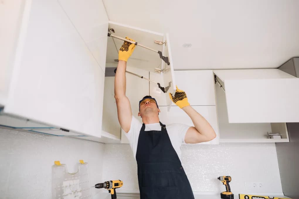 Man working on renovations in kitchen by installing cabinets.